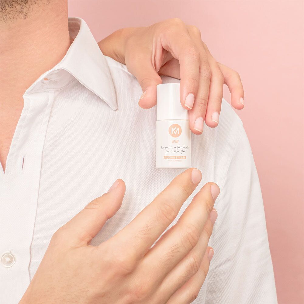 Eine weiße Flasche wird von zwei Händen gehalten. Aufschrift: MÊME, La solution fortifiante pour les ongles, Silicium et Urée.
