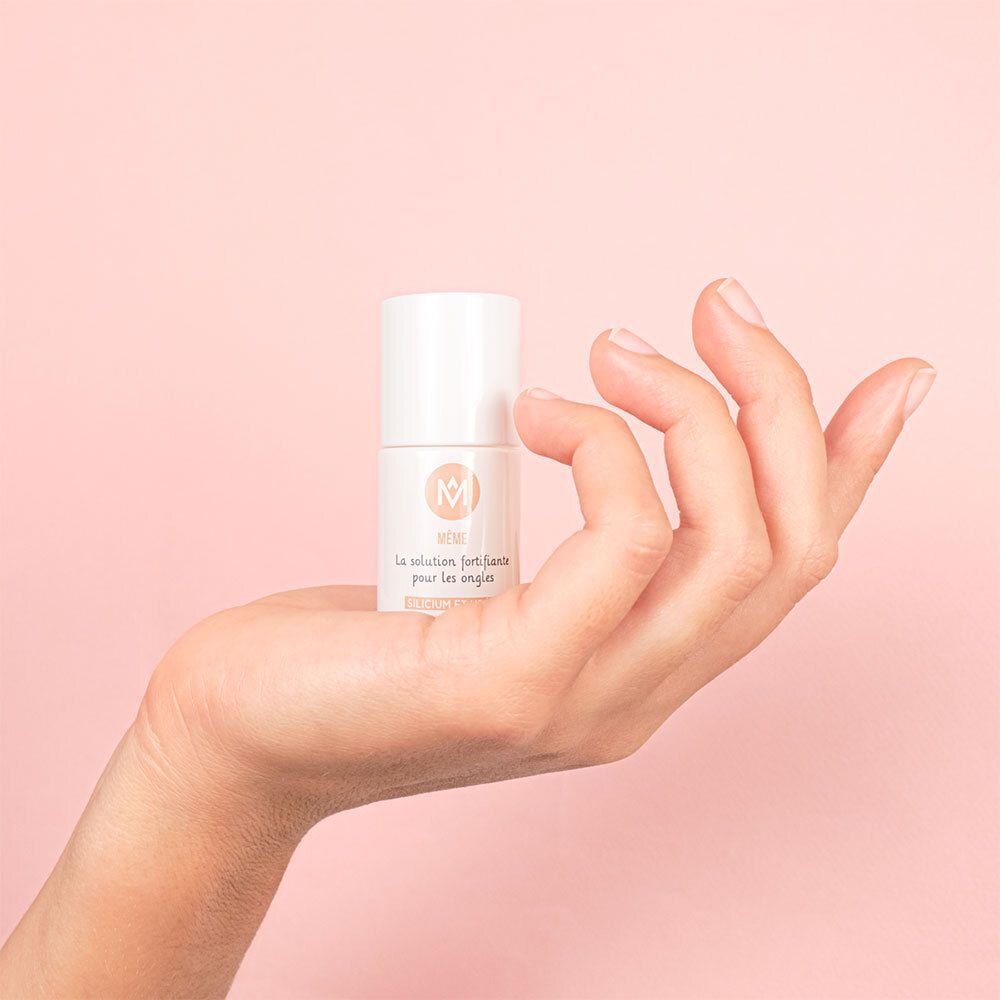 Eine weiße Flasche in einer Hand. Aufschrift: MÊME, La solution fortifiante pour les ongles, Silicium et Urée.