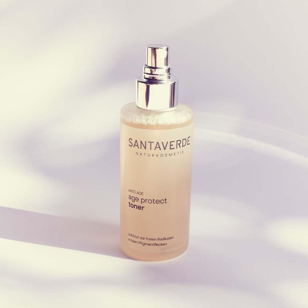 SANTAVERDE age protect toner Sprühflasche. Klare Flüssigkeit in einer Glasflasche mit silbernem Sprühkopf. Produktetikett mit Text.