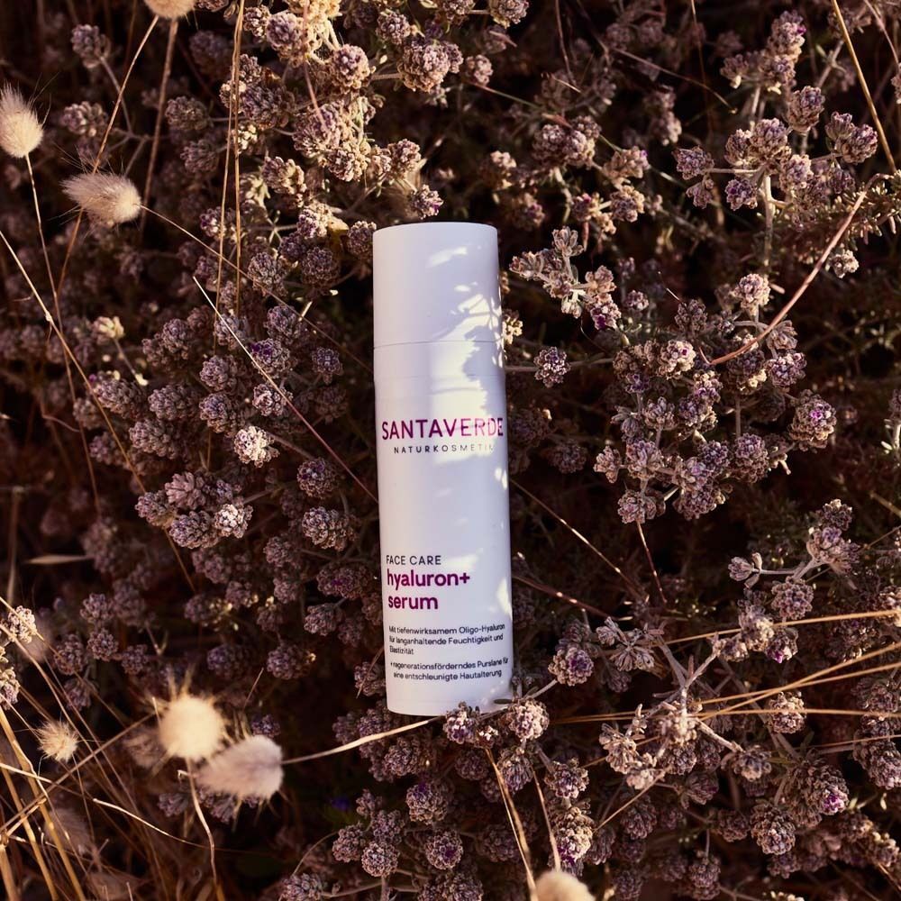 Weiße Flasche SANTAVERDE FACE CARE hyaluron+ serum auf Pflanzen. Text: ohne Duft. Mit tiefenwirksamem Oligo-Hyaluron für Feuchtigkeit und Elastizität.