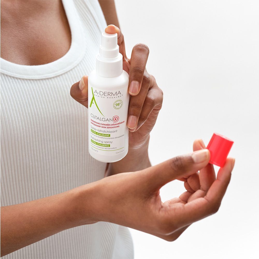 Person hält weiße Sprühflasche mit rotem Verschluss. Aufschrift: A-DERMA, Cutalgan, Spray rafraîchissant. Roter Verschluss in der anderen Hand.