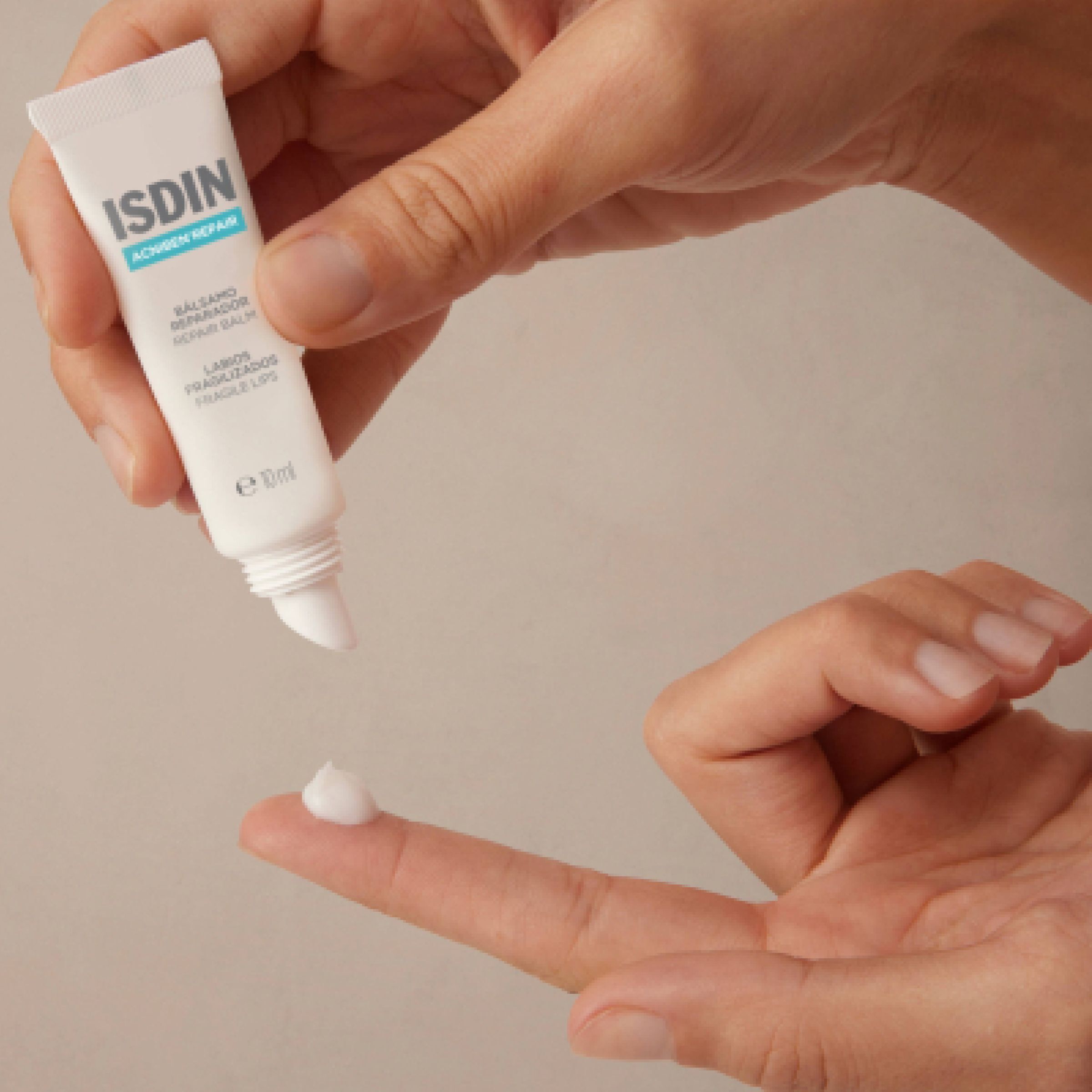 Eine Hand drückt eine kleine Menge ISDIN Acniben Repair Lippenbalsam aus einer Tube.