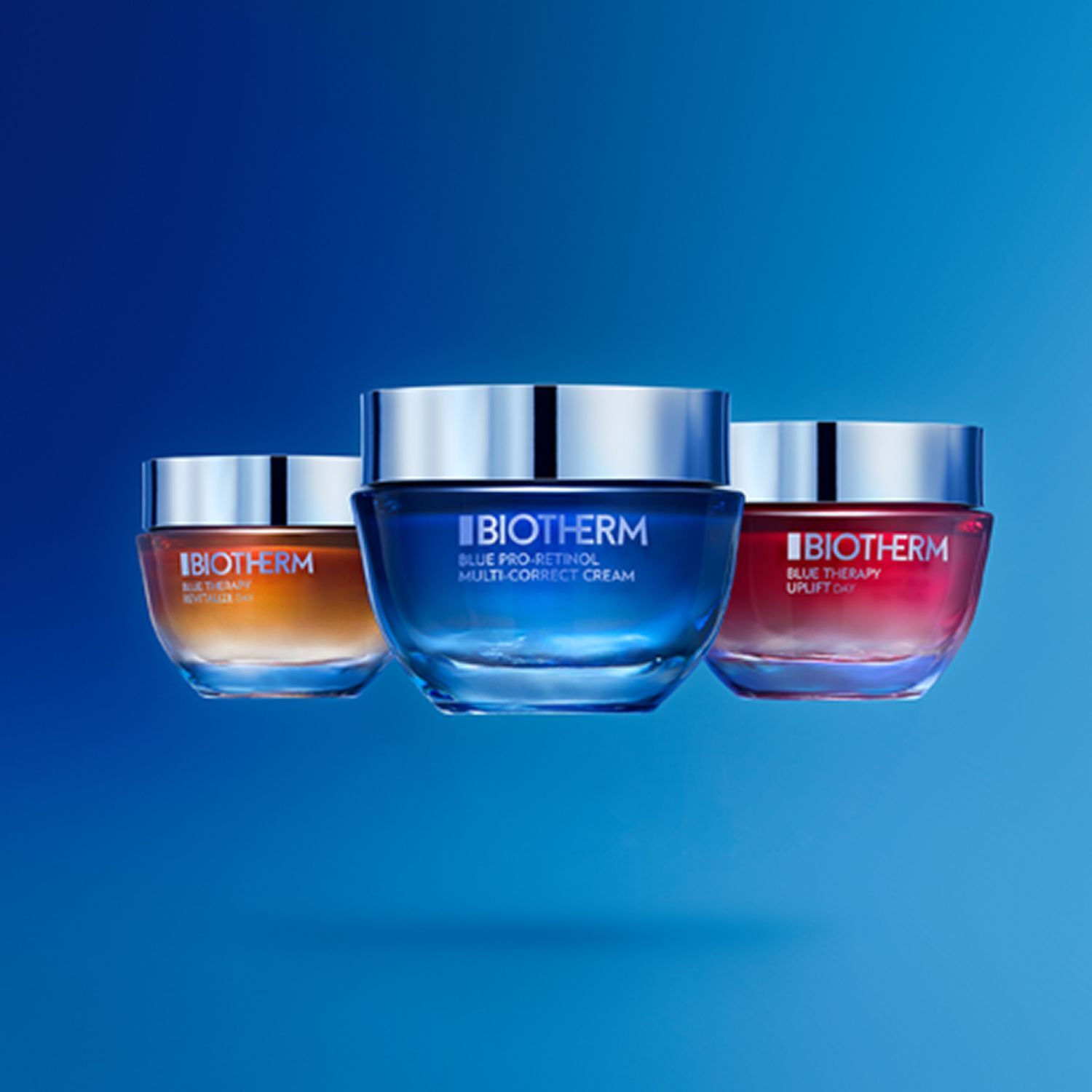 Drei Tiegel BIOTHERM Blue Therapy. Blau, orange und rot. Silberne Deckel. Auf blauem Hintergrund.