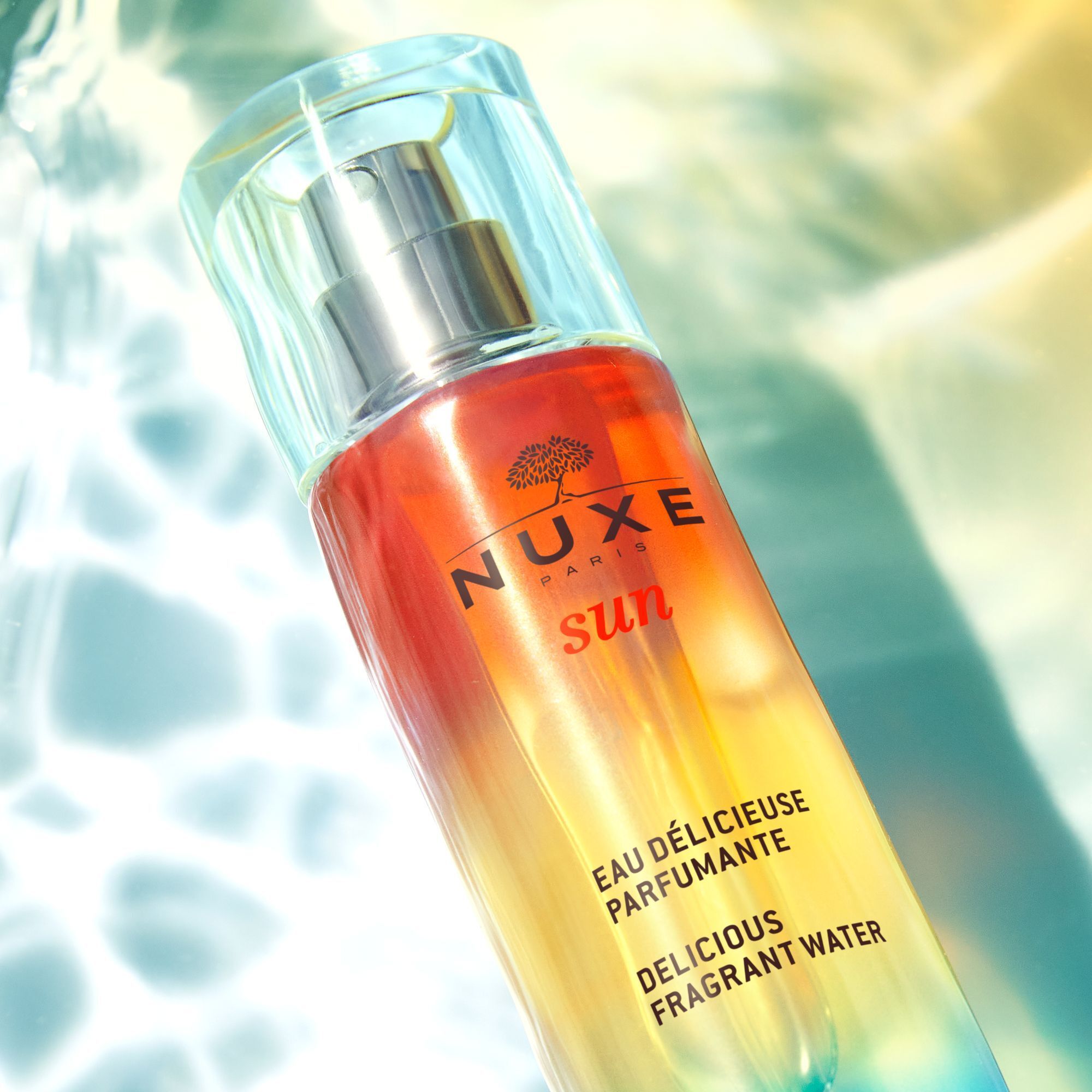 NUXE Sun Eau Délicieuse Parfumante. Flakon im Wasser. Produktname und Logo sichtbar.