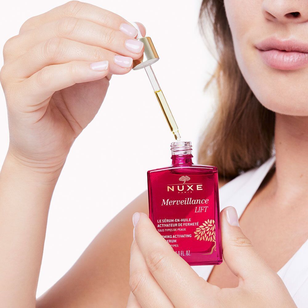 Eine Frau hält eine rosa Flasche NUXE Merveillance Lift. Eine Pipette wird in die Flasche eingeführt. Text: Merveillance Lift, Öl-Serum.