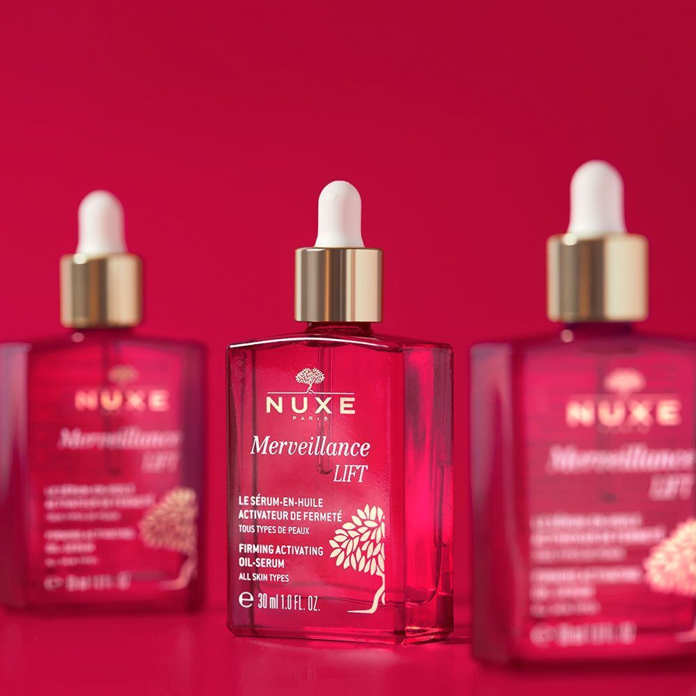 Drei Flaschen NUXE Merveillance Lift Öl-Serum auf rotem Hintergrund. Rosa Glasflaschen mit goldenen Verschlüssen und weißen Pipetten. Text: Merveillance Lift.