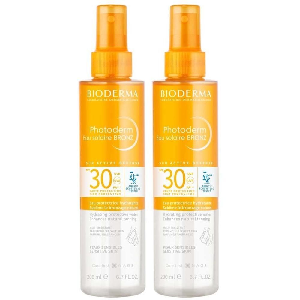 Zwei Sprays BIODERMA Photoderm Eau solaire BRONZ SPF 30. Orangefarbene Sprühköpfe, transparente Flaschen. Text: Photoderm, SPF 30, 200 ml.