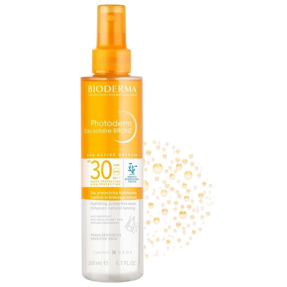 BIODERMA Photoderm Eau solaire BRONZ SPF 30 Spray. Orangefarbener Sprühkopf, transparente Flasche. Text: Photoderm, SPF 30, 200 ml. Wasserblasen im Hintergrund.