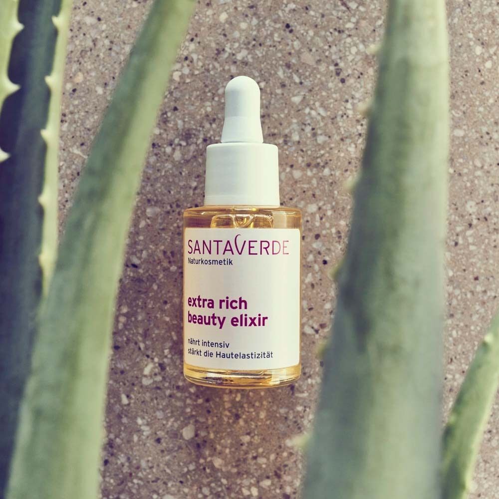 SANTAVERDE Gesichtsöl-Flasche mit Pipette, umgeben von Aloe Vera Blättern. Aufschrift: extra rich beauty elixir.