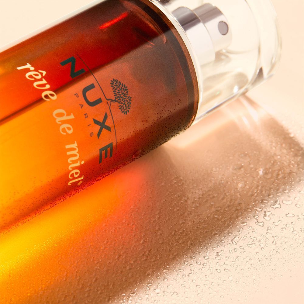 Flakon mit Sprühkopf, liegend. Aufschrift: NUXE Reve de Miel. Farbverlauf von bernsteinfarben nach transparent.