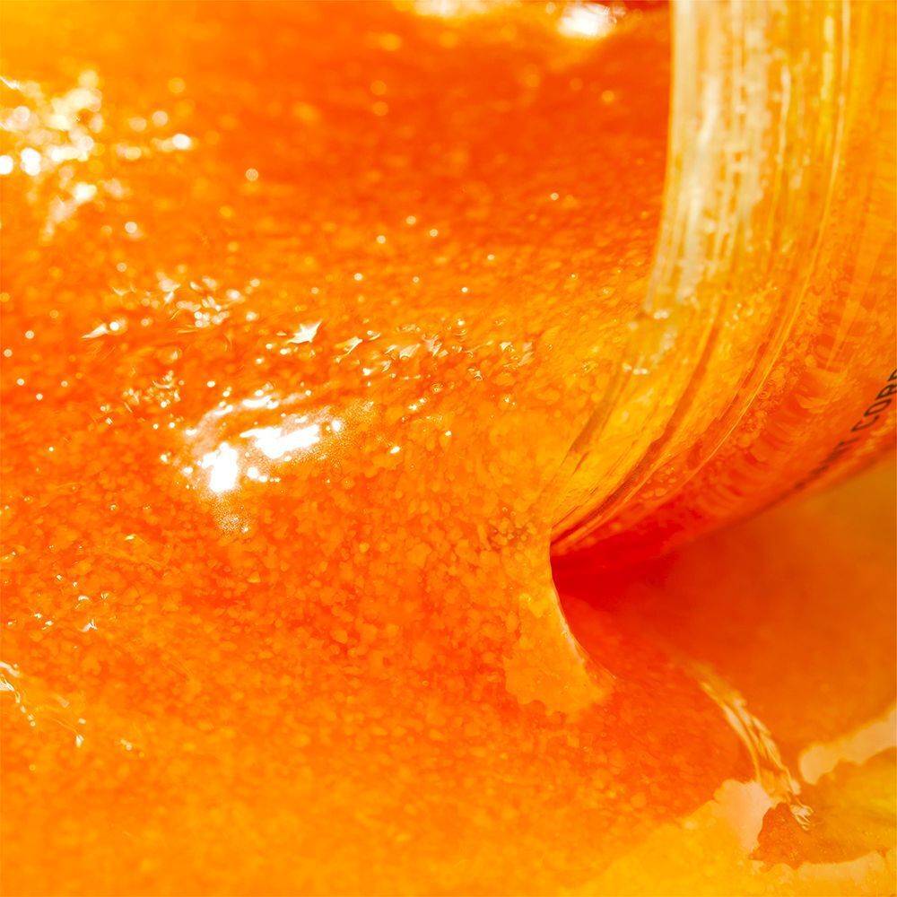Nahaufnahme von Körperpeeling, das aus einem Tiegel gegossen wird. Orangefarbenes Produkt.