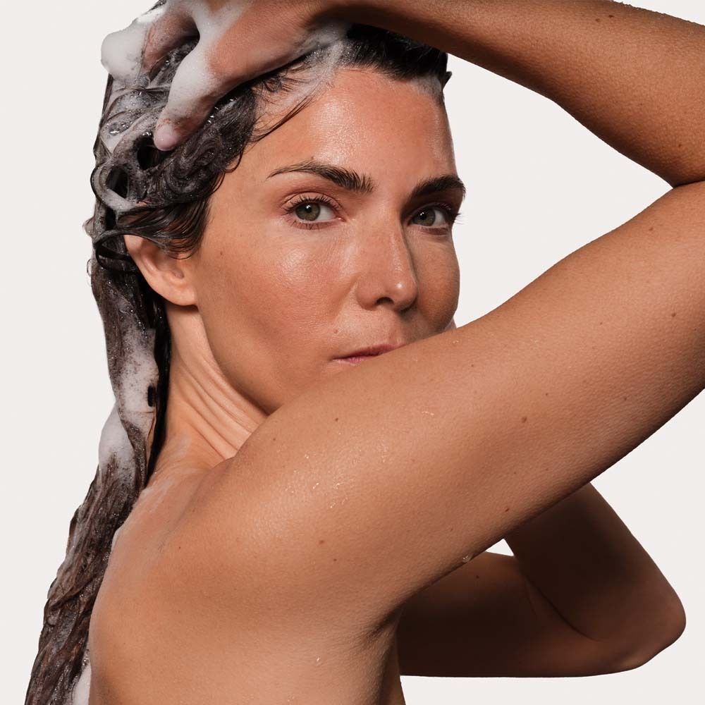 Frau wäscht sich die Haare mit Shampoo. Schaum auf dem Haar. Blick in die Kamera. Helle Haut.