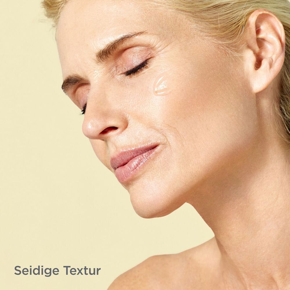 Gesicht einer Frau. Text: Seidige Textur. Gelbe Flüssigkeit auf der Haut. Geschlossene Augen.