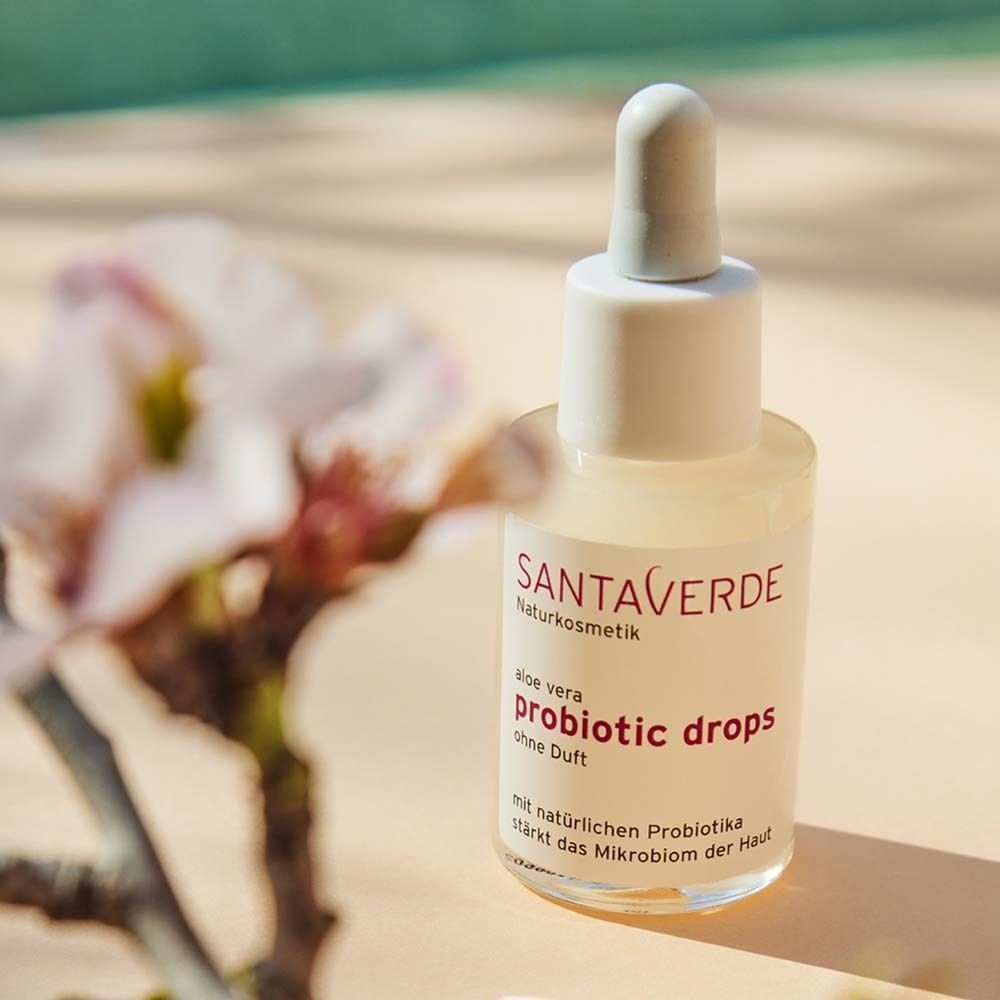 SANTAVERDE PROBIOTIC drops Flasche. Weiße Flasche mit Dosierpipette. Aufschrift: SANTAVERDE, probiotic drops, ohne Duft. Hintergrund: Blüten.