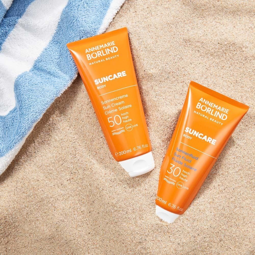 Zwei Tuben Sonnencreme auf Sand und Handtuch. Aufschrift: ANNEMARIE BÖRLIND, SUNCAR, LSF 50 und LSF 30.