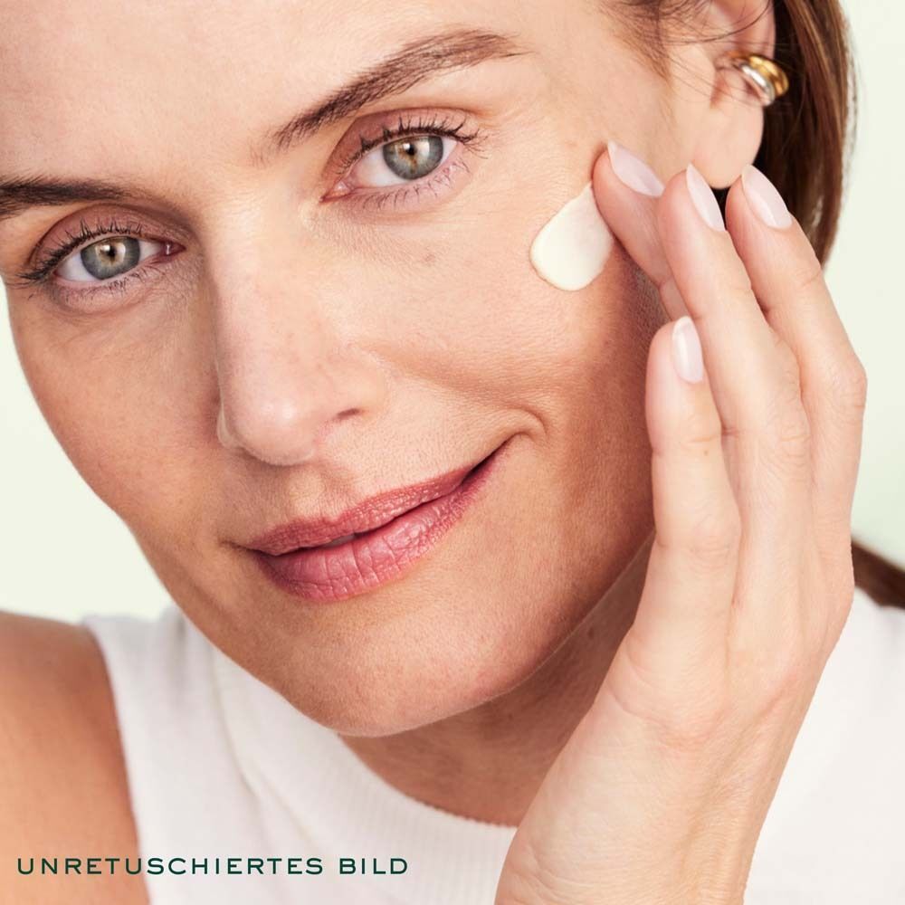 Nahaufnahme einer Frau, die Creme auf ihr Gesicht aufträgt. Aufschrift: UNRETUSCHIERTES BILD.