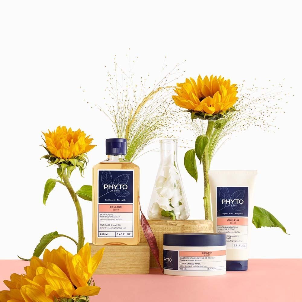 Produkt-Arrangement mit Shampoo, Creme und Sonnenblumen. Aufschrift: PHYTO PARIS, COLOR. Auf rosa Untergrund.