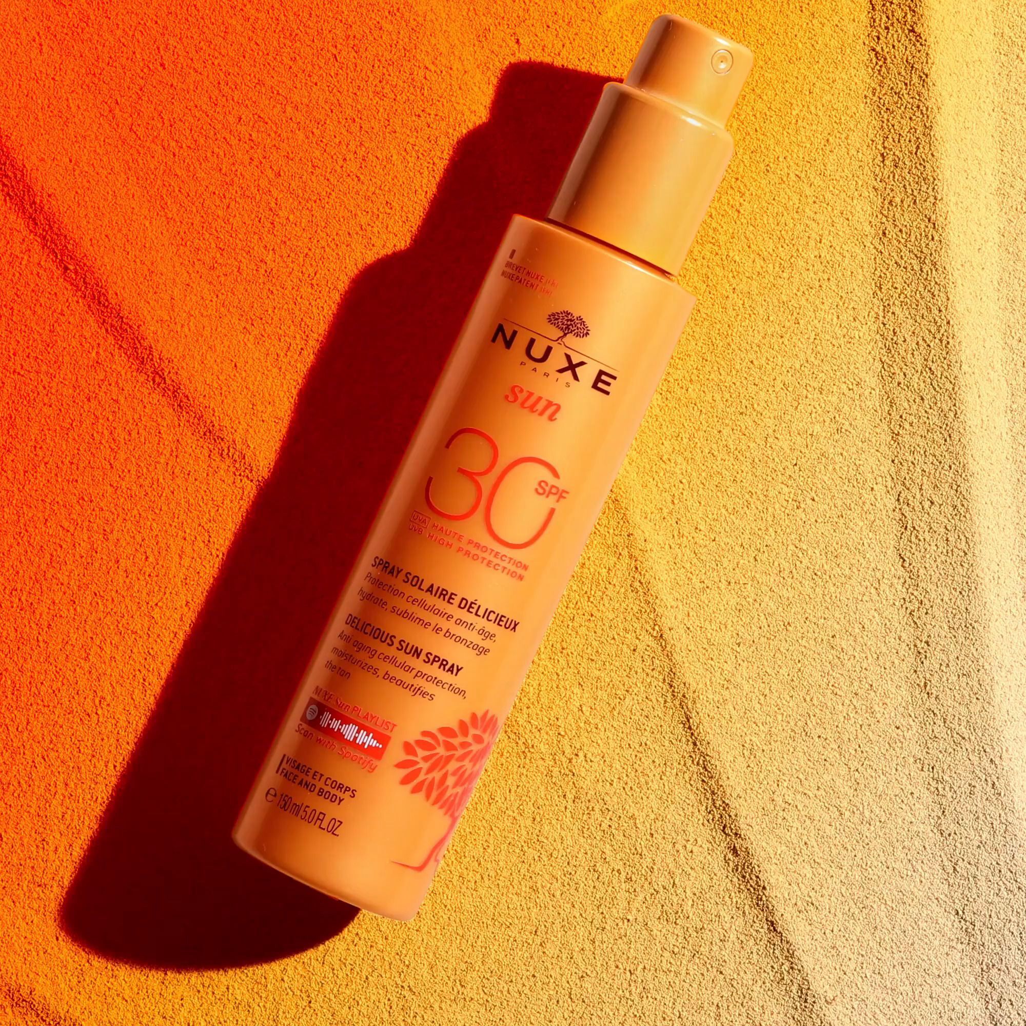 Sonnencreme-Flasche auf gelbem Handtuch. Aufschrift NUXE Sun, SPF 30. Text: Delicious Sun Spray.