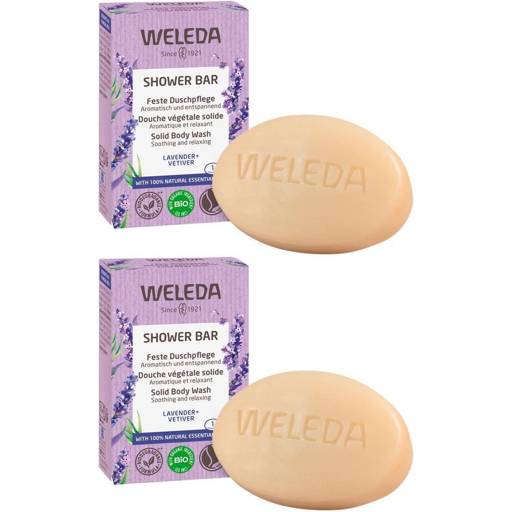 Zwei ovale Seifen und zwei lilafarbene Kartons mit Produktinformationen. Auf den Kartons steht "WELEDA SHOWER BAR".