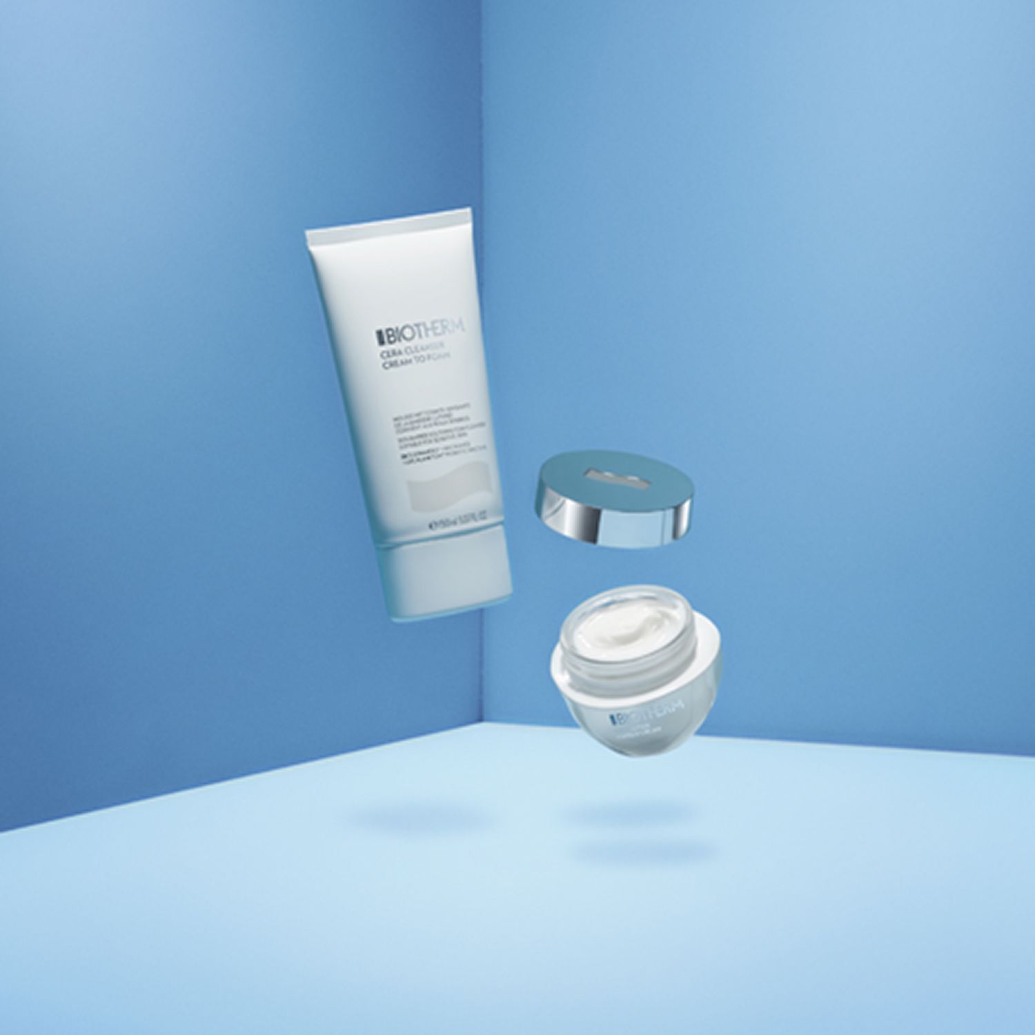 Eine weiße Tube und ein Tiegel mit Deckel schweben vor blauem Hintergrund. Aufschrift: BIOTHERM Cera Cleanser Cream to Foam.