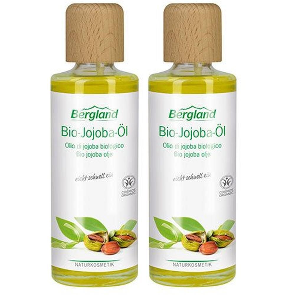 Zwei Flaschen Bergland Bio-Jojoba-Öl. Glasflaschen mit Holzdeckel. Etikett mit Produktnamen, Blättern und Jojobasamen. Naturkosmetik.