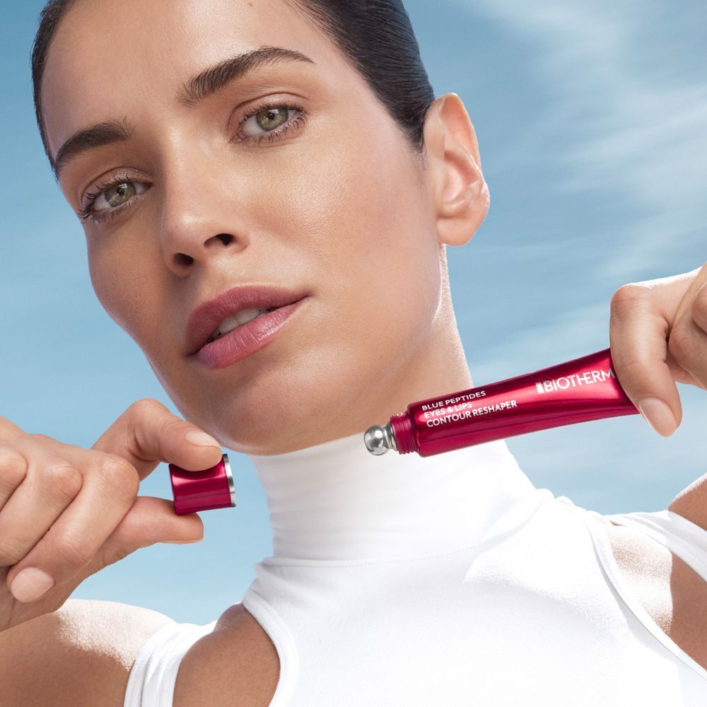 Frau hält eine rote Tube. Produktname: BLUE PEPTIDES EYES & LIPS CONTOUR RESHAPER. BIOTHERM-Logo.