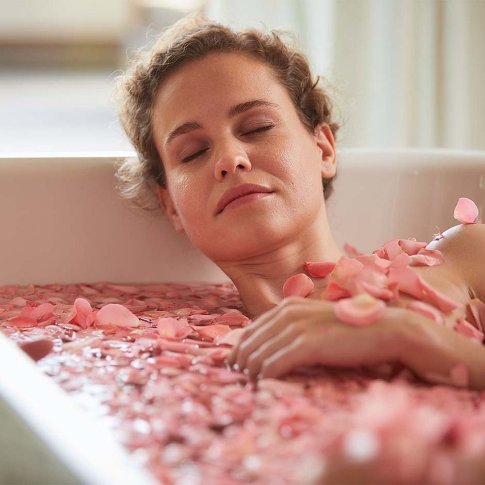 Eine Frau liegt in einer Badewanne mit Rosenblättern.