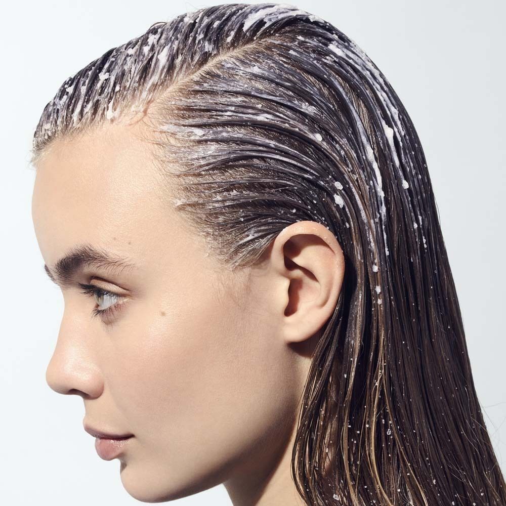 Profil einer Frau mit aufgetragenem Peeling auf dem Haaransatz. Haare sind nass und mit Produkt bedeckt. Helle Haut.