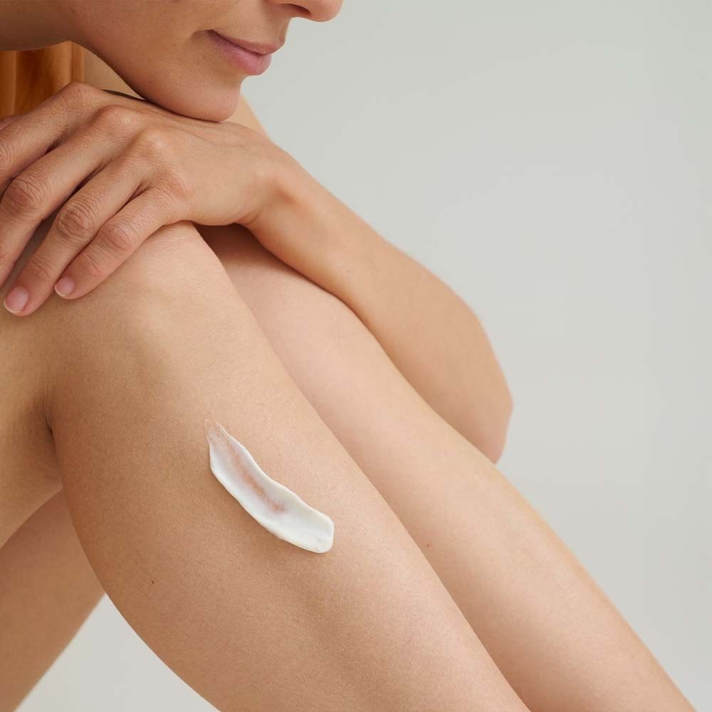 Nahaufnahme einer Person, die Creme auf ihr Bein aufträgt. Weiße Creme auf der Haut. Helle Hautfarbe.