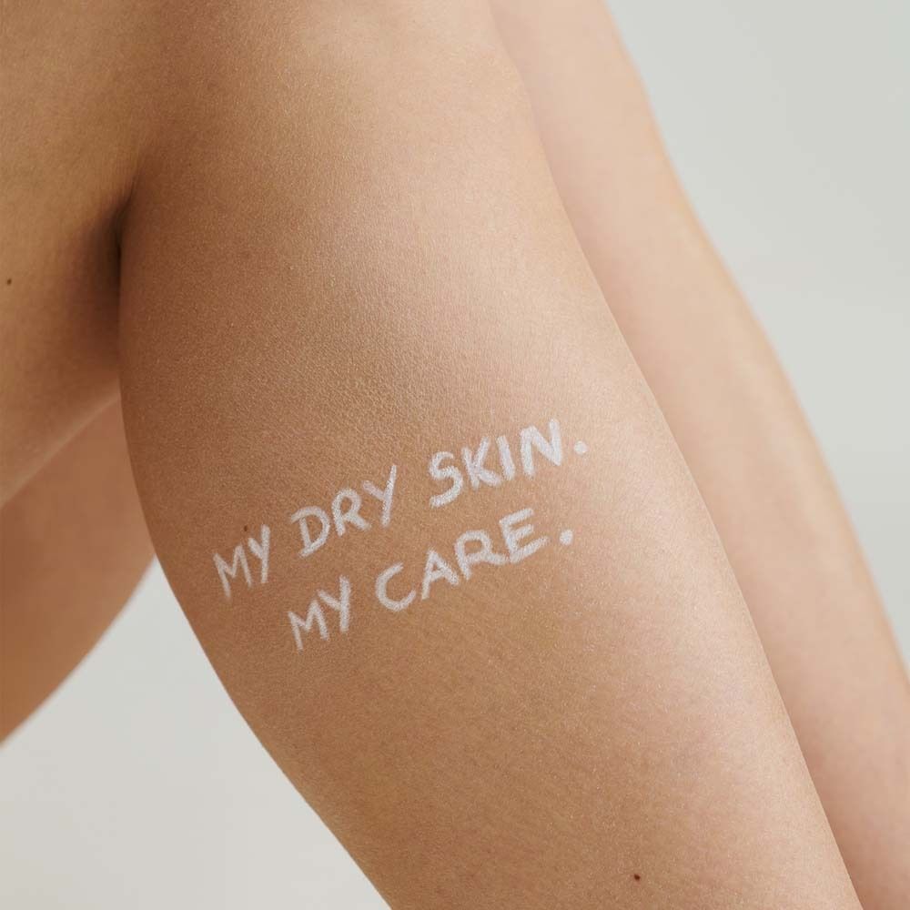 Arm einer Person mit dem Text „MY DRY SKIN. MY CARE.“ in weißer Schrift auf der Haut.
