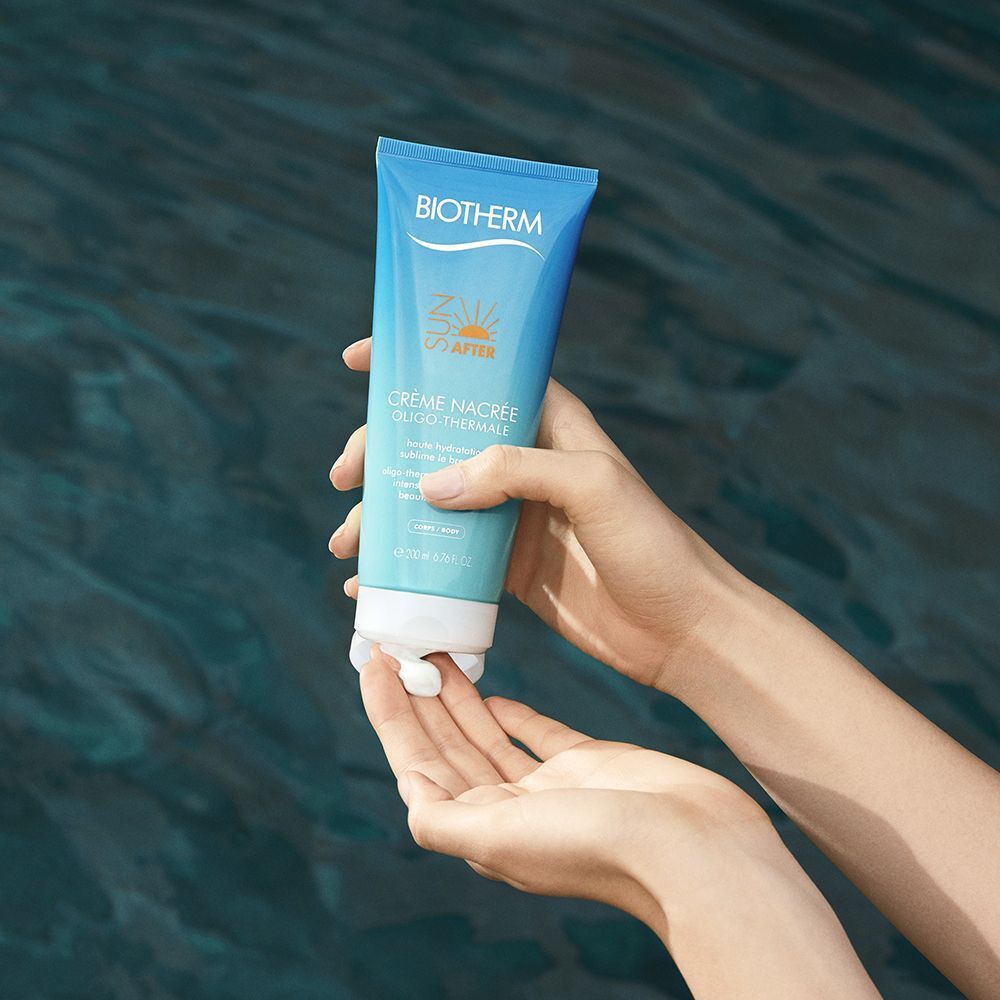 Person hält Tube BIOTHERM Crème Nacrée After Sun. Türkis-blaue Tube mit weißem Verschluss. Creme wird auf die Hand aufgetragen.