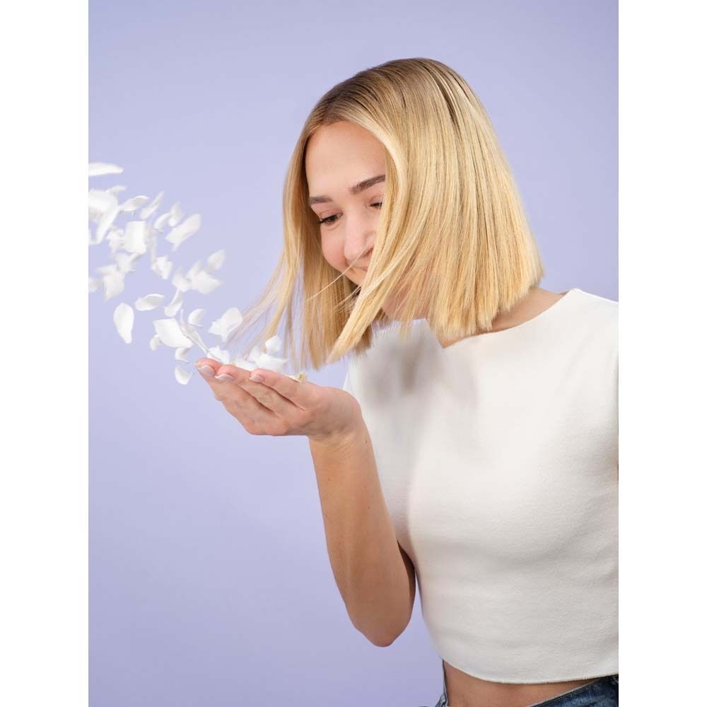 Eine Frau mit blonden Haaren, die Blütenblätter in die Luft wirft. Hintergrund: hellviolett.