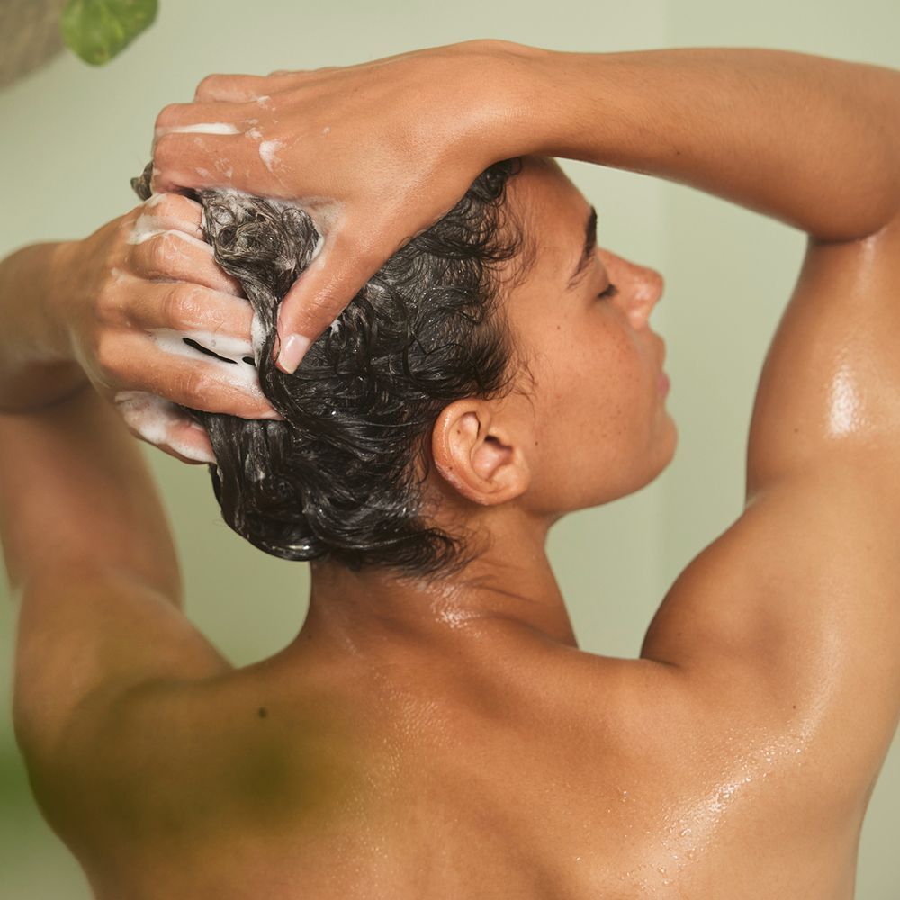 Person wäscht sich die Haare unter der Dusche. Schaum auf dem Kopf. Rückansicht.