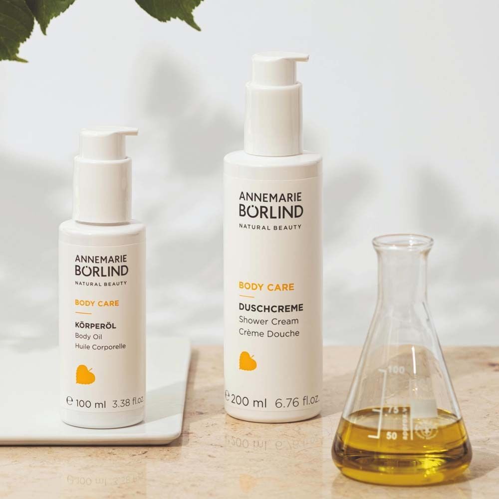 Zwei Annemarie Börlind Körperpflegeprodukte: Körneröl (100ml) und Duschcreme (200ml). Daneben ein Becherglas mit gelblicher Flüssigkeit.