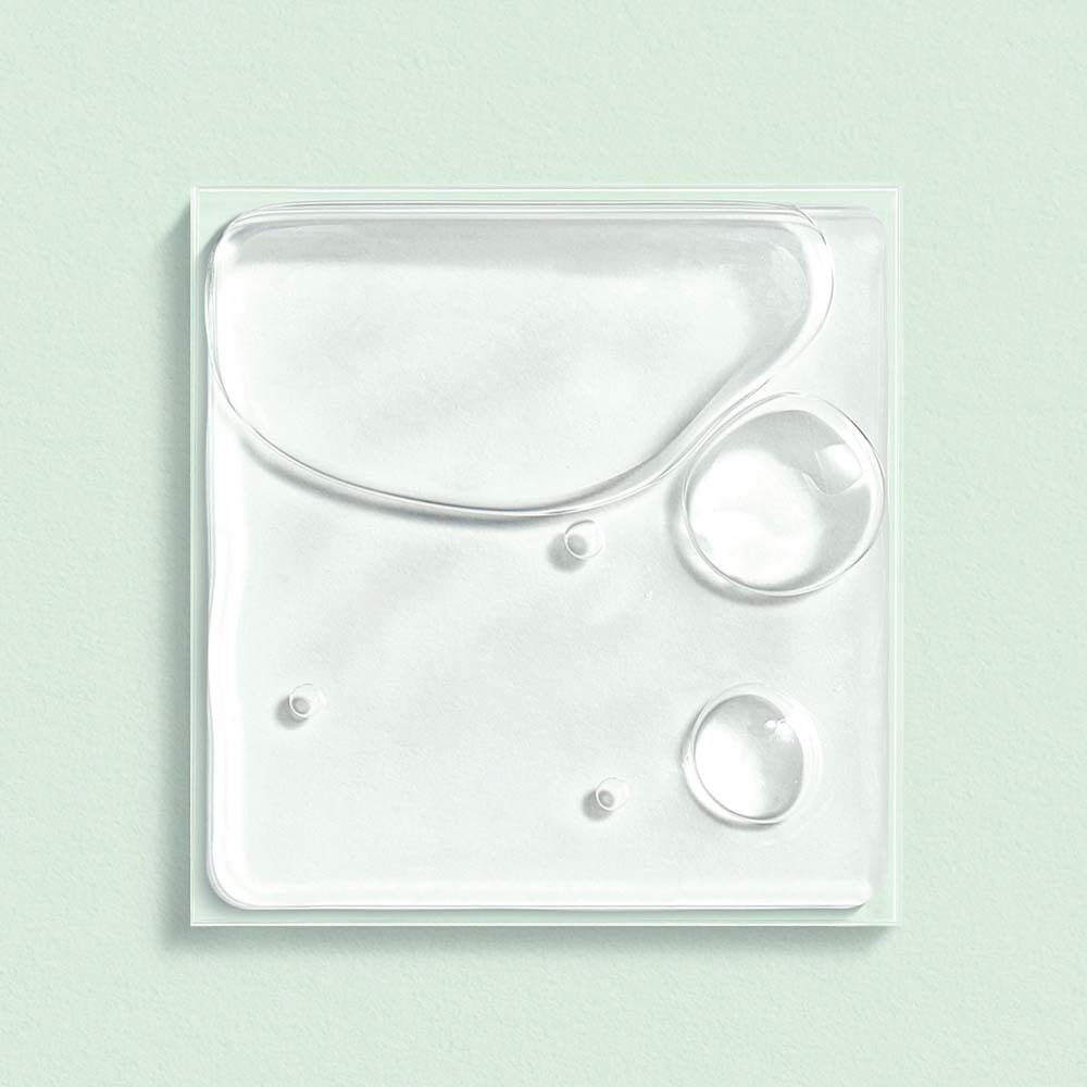 Nahaufnahme von transparenten Flüssigkeitstropfen auf einer quadratischen, weißen Oberfläche. Einige kleine Blasen.
