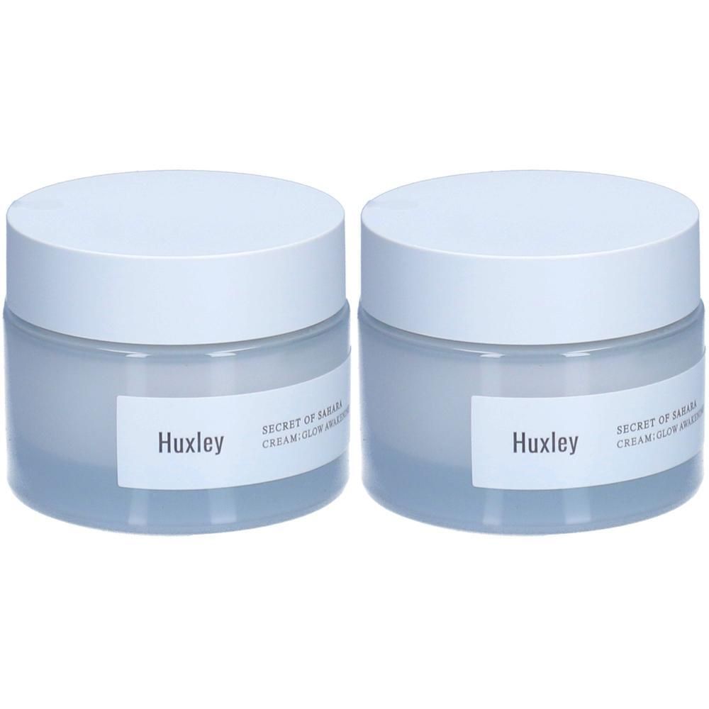 Zwei Cremetiegel mit weißen Deckeln. Auf den Etiketten steht "Huxley" und "SECRET OF SAHARA CREAM; GLOW AWAKENING".