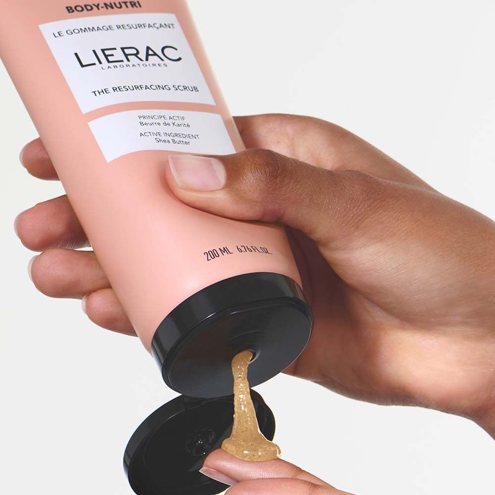 Hand hält Tube Körperpeeling. Produkt wird auf Finger gedrückt. Text: BODY-NUTRI, LIERAC, THE RESURFACING SCRUB, 200 ml.