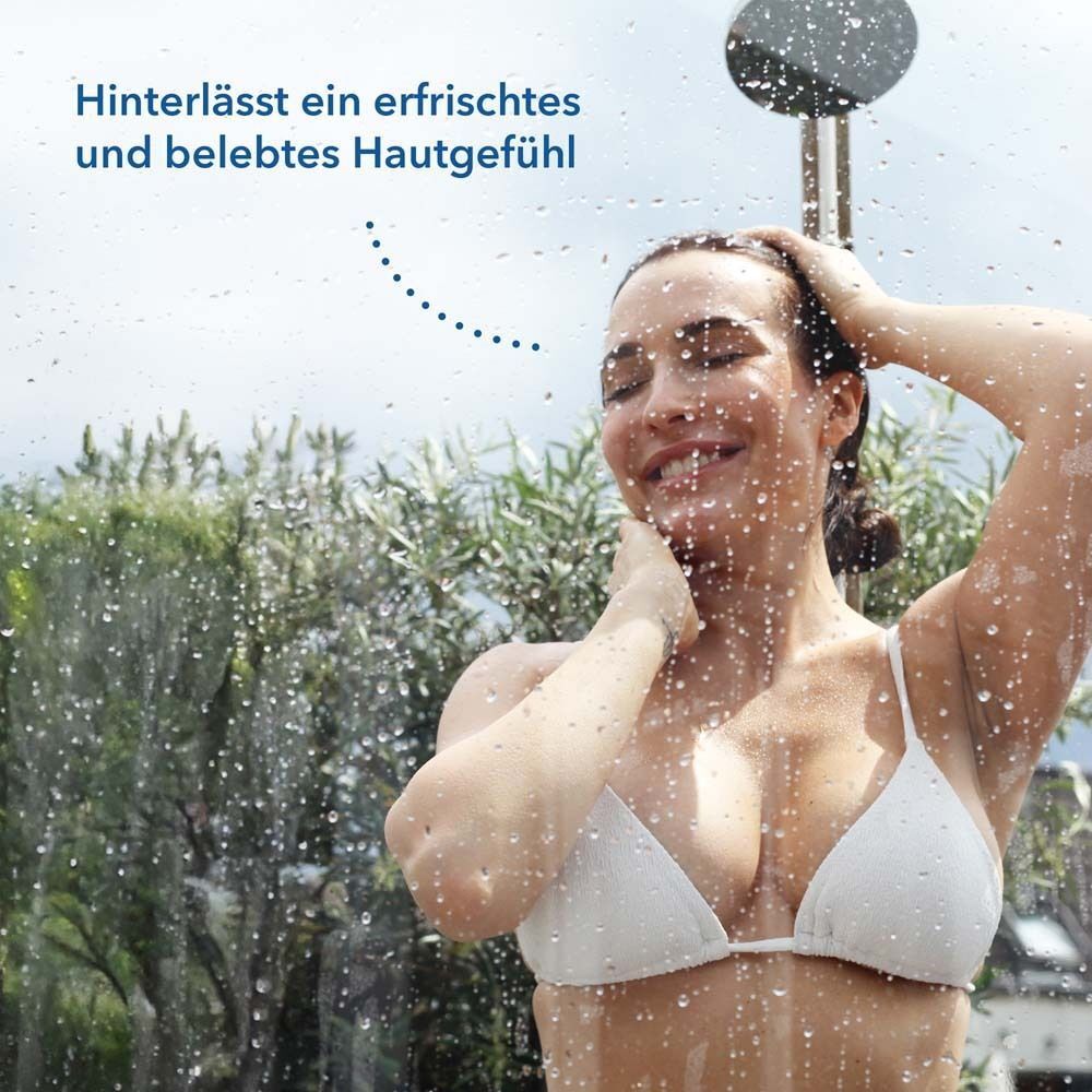 Frau unter der Dusche. Wasser fließt über sie. Text: Hinterlässt ein erfrischtes und belebtes Hautgefühl.