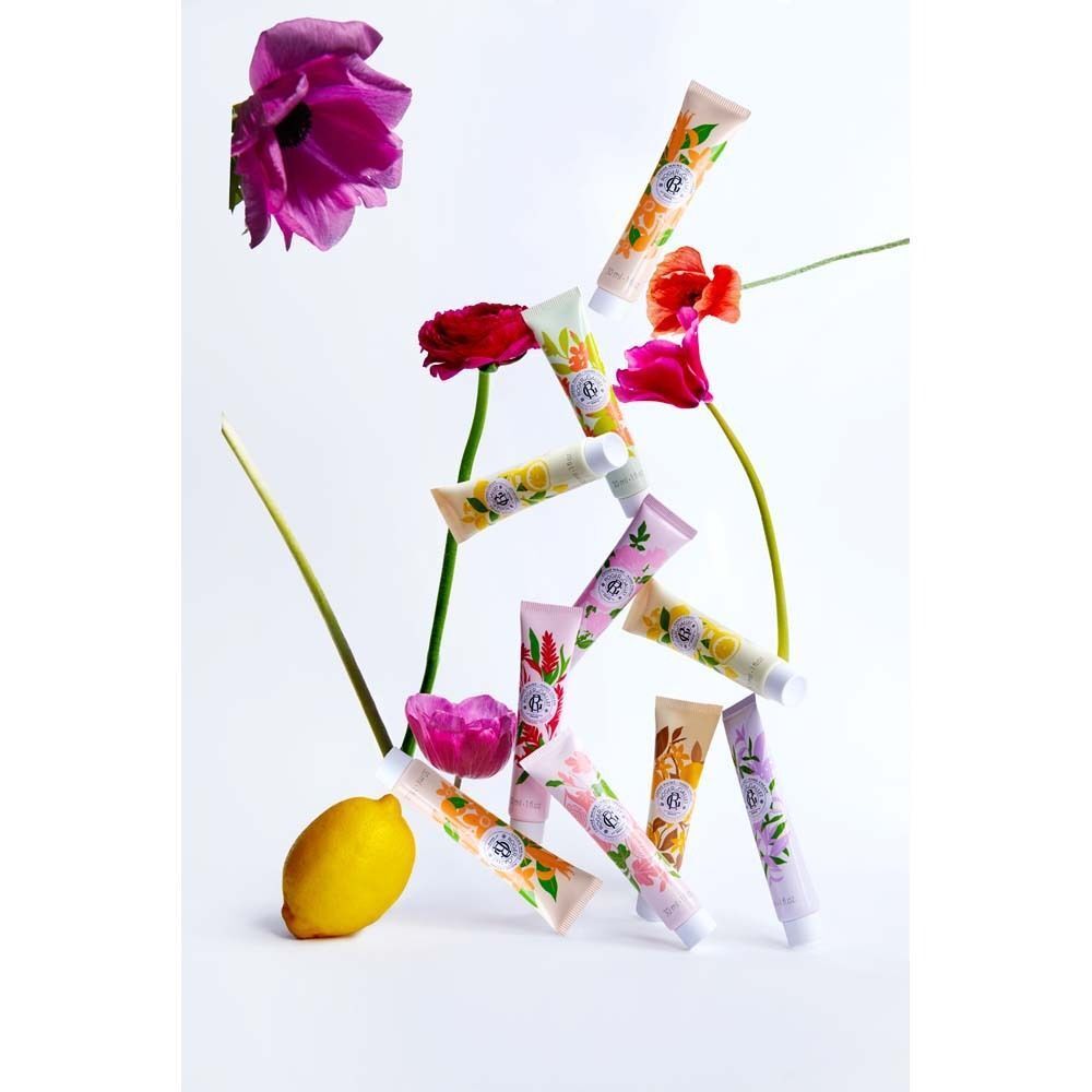 Mehrere Tuben Handcreme, arrangiert mit Blumen und einer Zitrone. Verschiedene Farben und Designs. Einige zeigen Aufschriften.