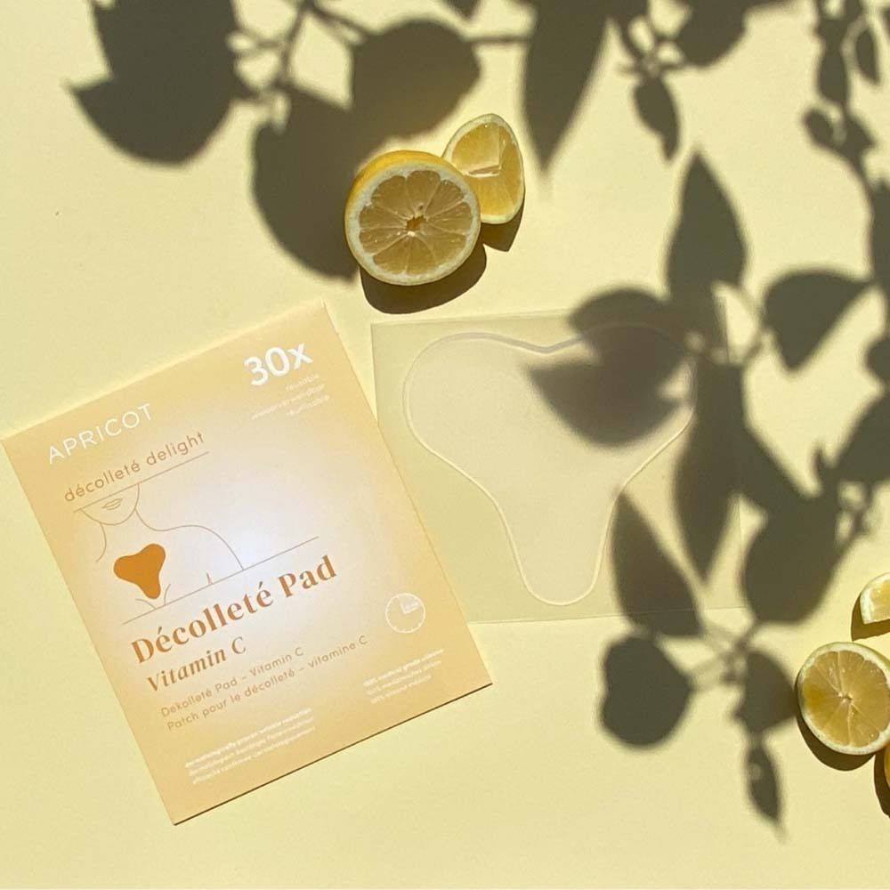 Karton und Dekolleté Pad neben Zitronen. Aufdruck: APRICOT, Décolleté Pad Vitamin C.