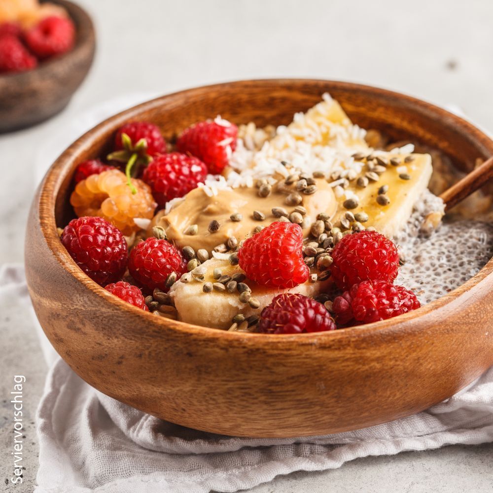 Holzschale mit Beeren, Banane und Samen. Auf weißem Tuch.