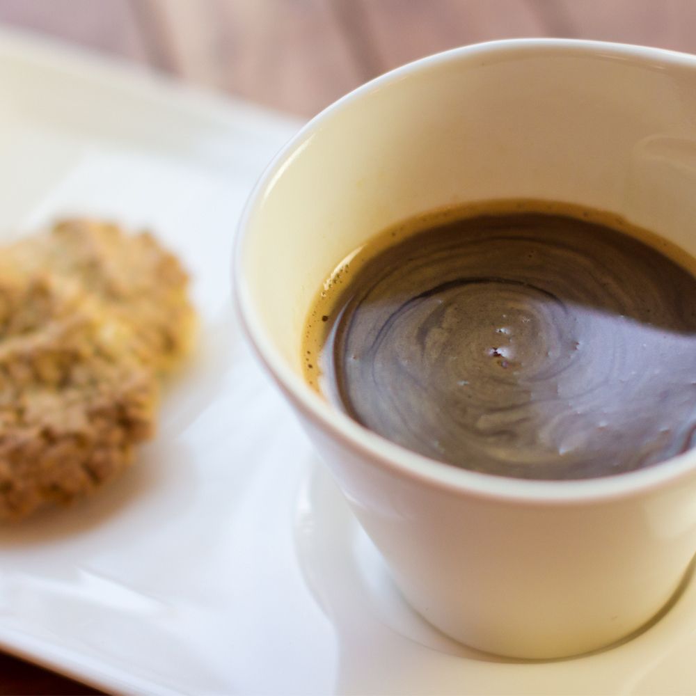Tasse Kaffee mit einem Keks auf einem weißen Teller.