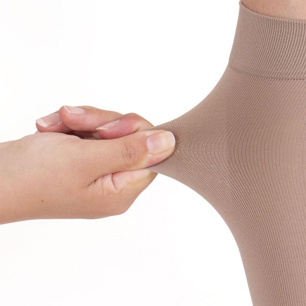 Hand dehnt den Stoff eines beigen Strumpfes. Der Stoff ist glatt und dehnbar. Keine weiteren Details sichtbar.