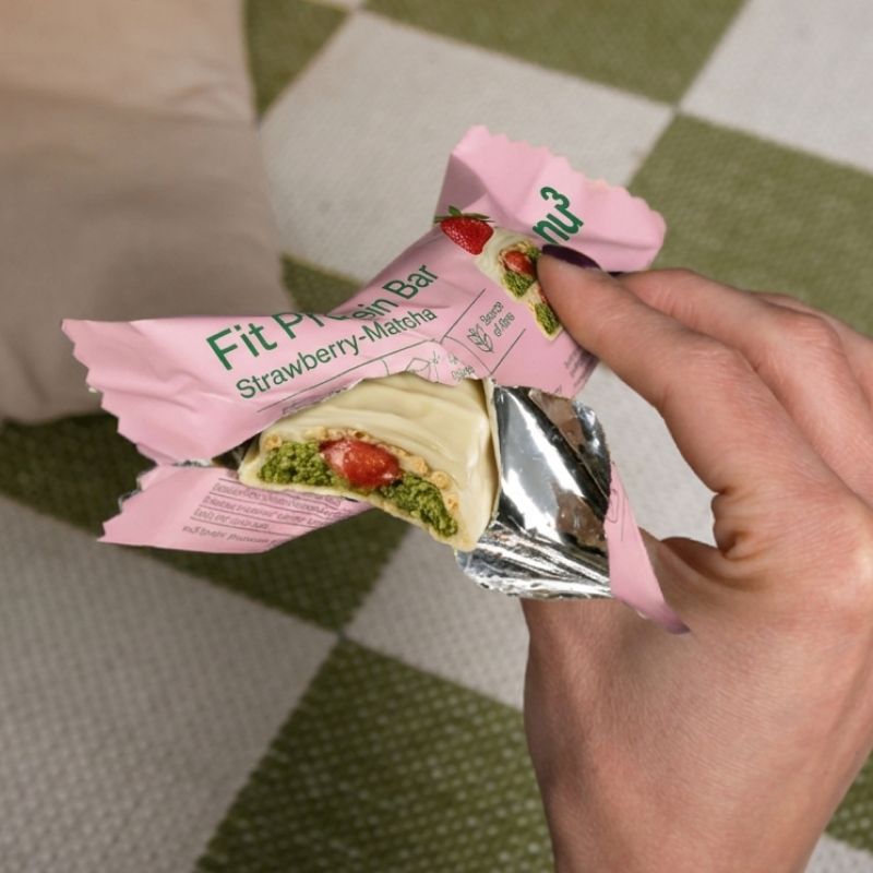 Eine Hand öffnet die Verpackung eines nu3 Fit Protein Riegels, Erdbeer-Matcha, mit Blick auf den Riegel.