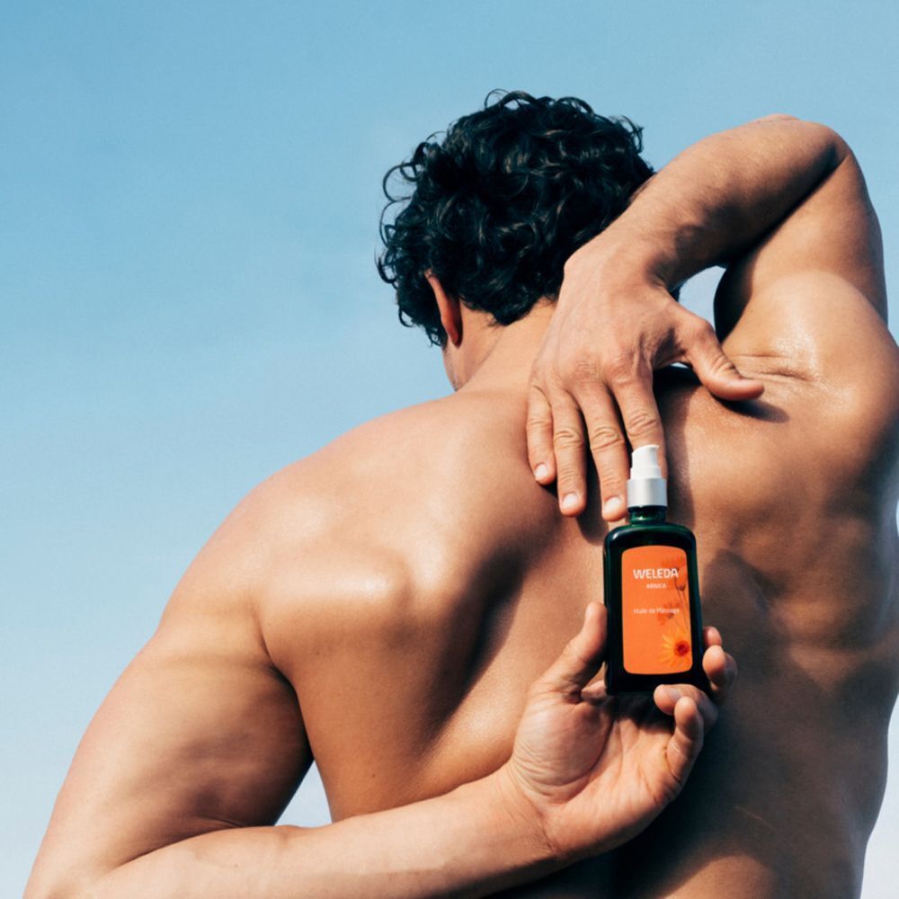 Mann hält Weleda Arnika Massageöl-Flasche hinter dem Rücken.