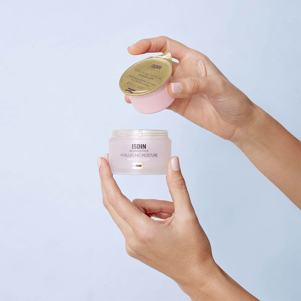 Hände öffnen einen ISDINCEUTICS Hyaluronic Moisture Tiegel. Heller rosa Tiegel mit goldfarbenem Innendeckel.