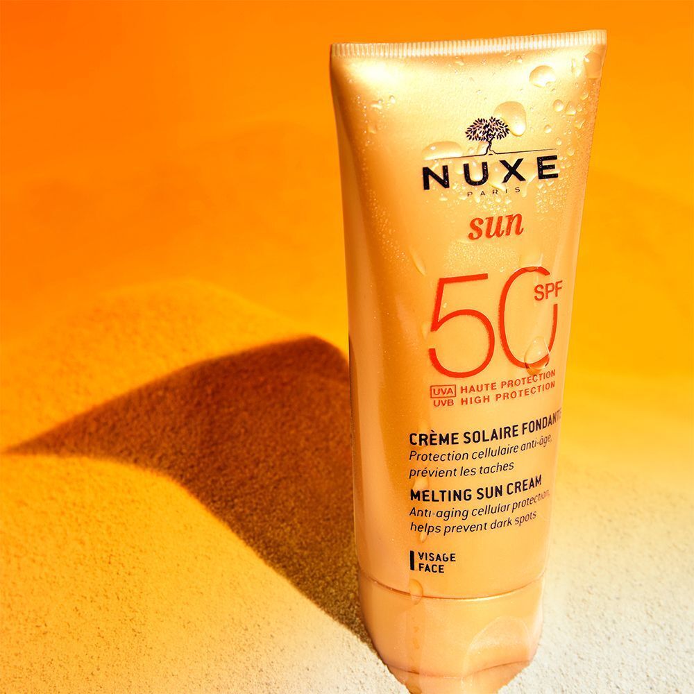 Nuxe Sun Sonnencreme Gesicht LSF 50 Tube auf sandigem Untergrund mit orangem Licht.