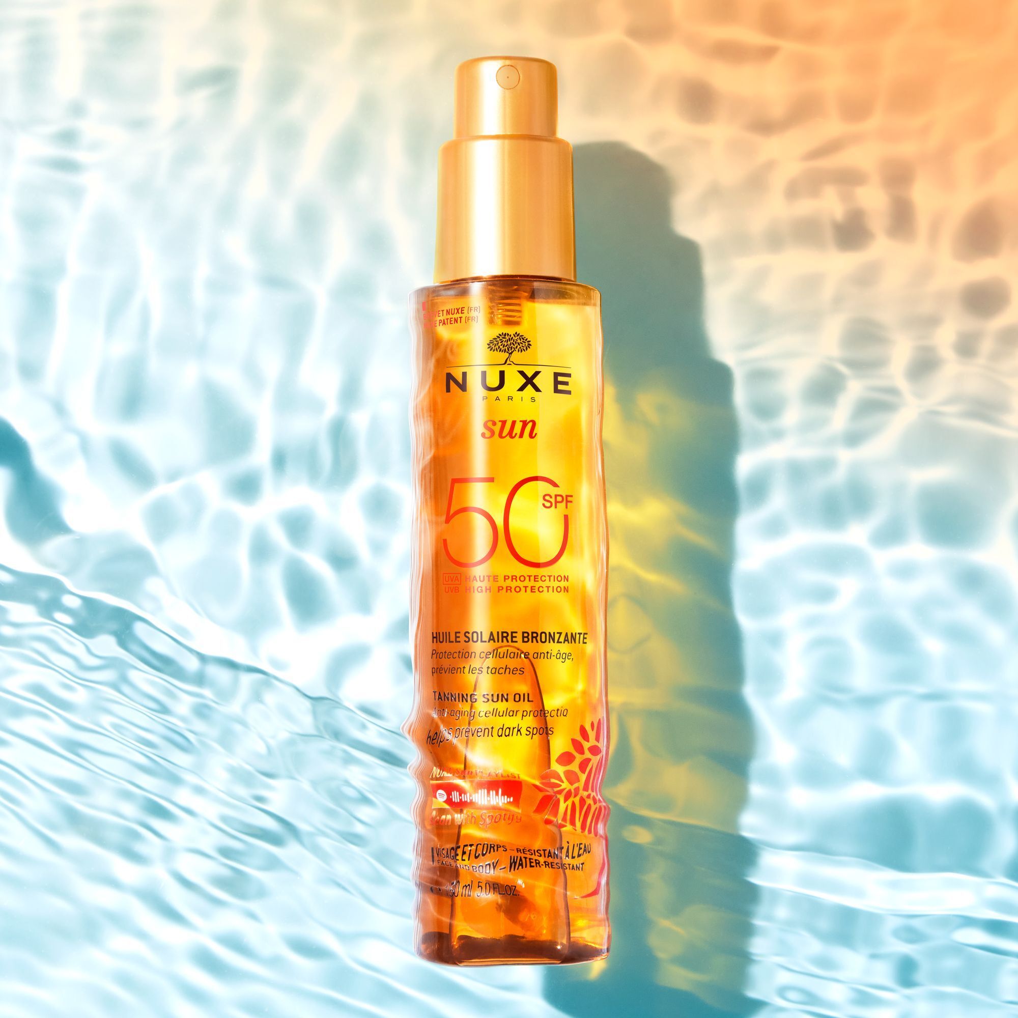 Flasche Nuxe Sun Sonnenöl LSF 50 über Wasser, mit reflektierendem Licht.