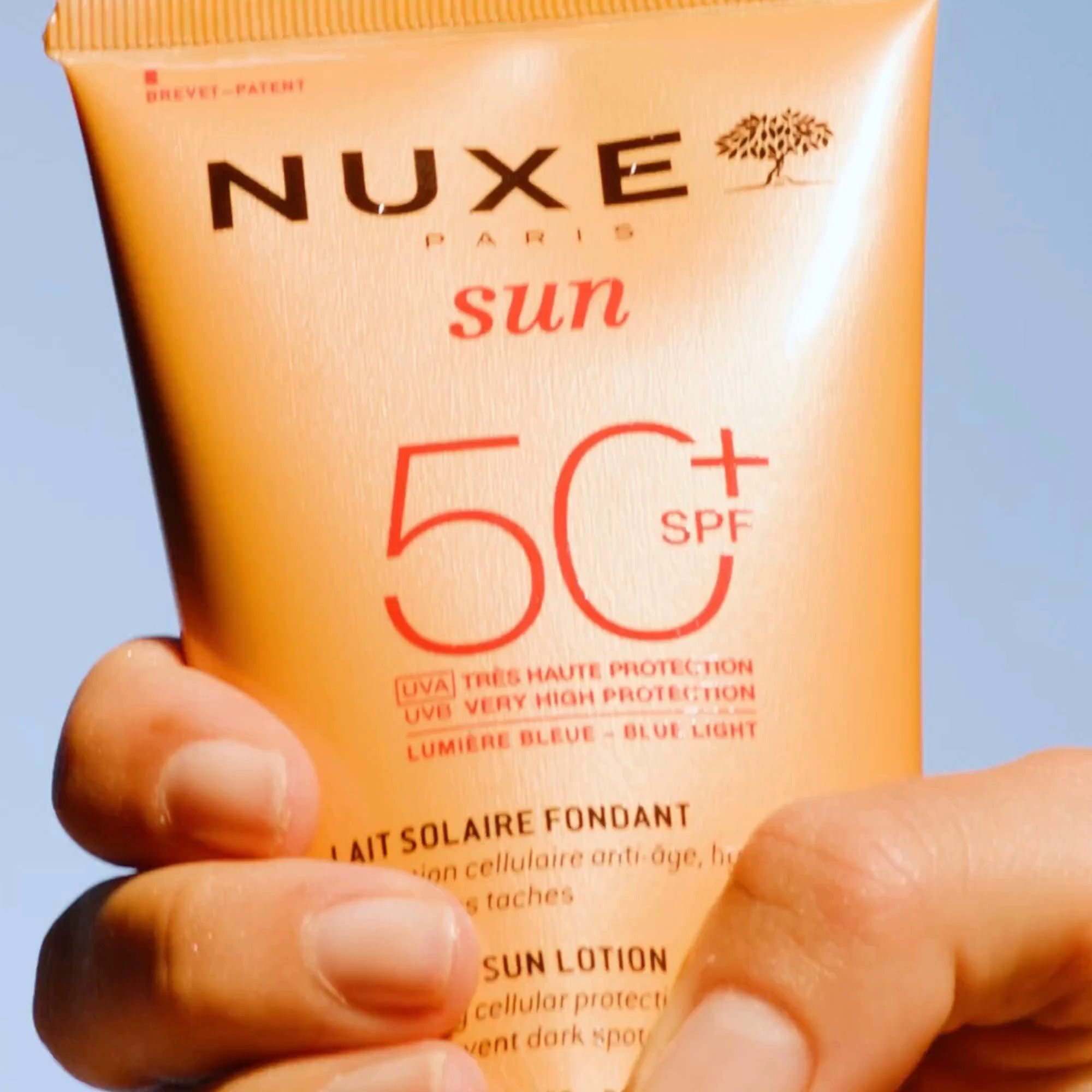Nahaufnahme einer Hand, die eine Nuxe Sonnenmilch Flasche mit LSF 50 hält.