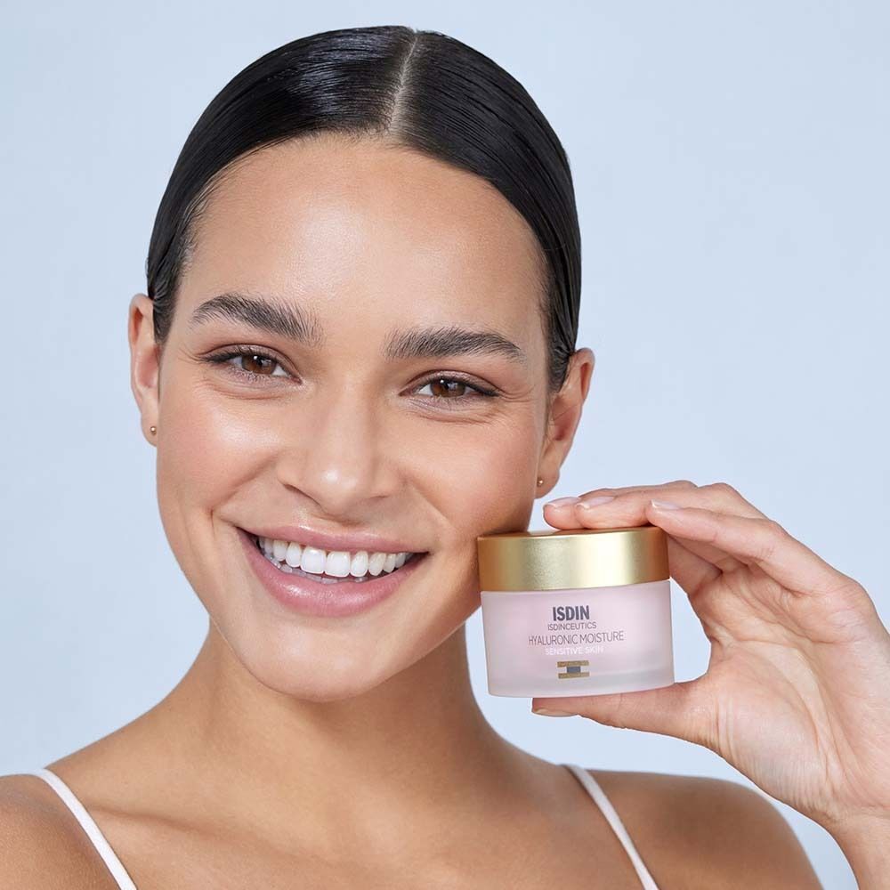 Lächelnde Frau hält einen ISDINCEUTICS Hyaluronic Moisture Cremetiegel.